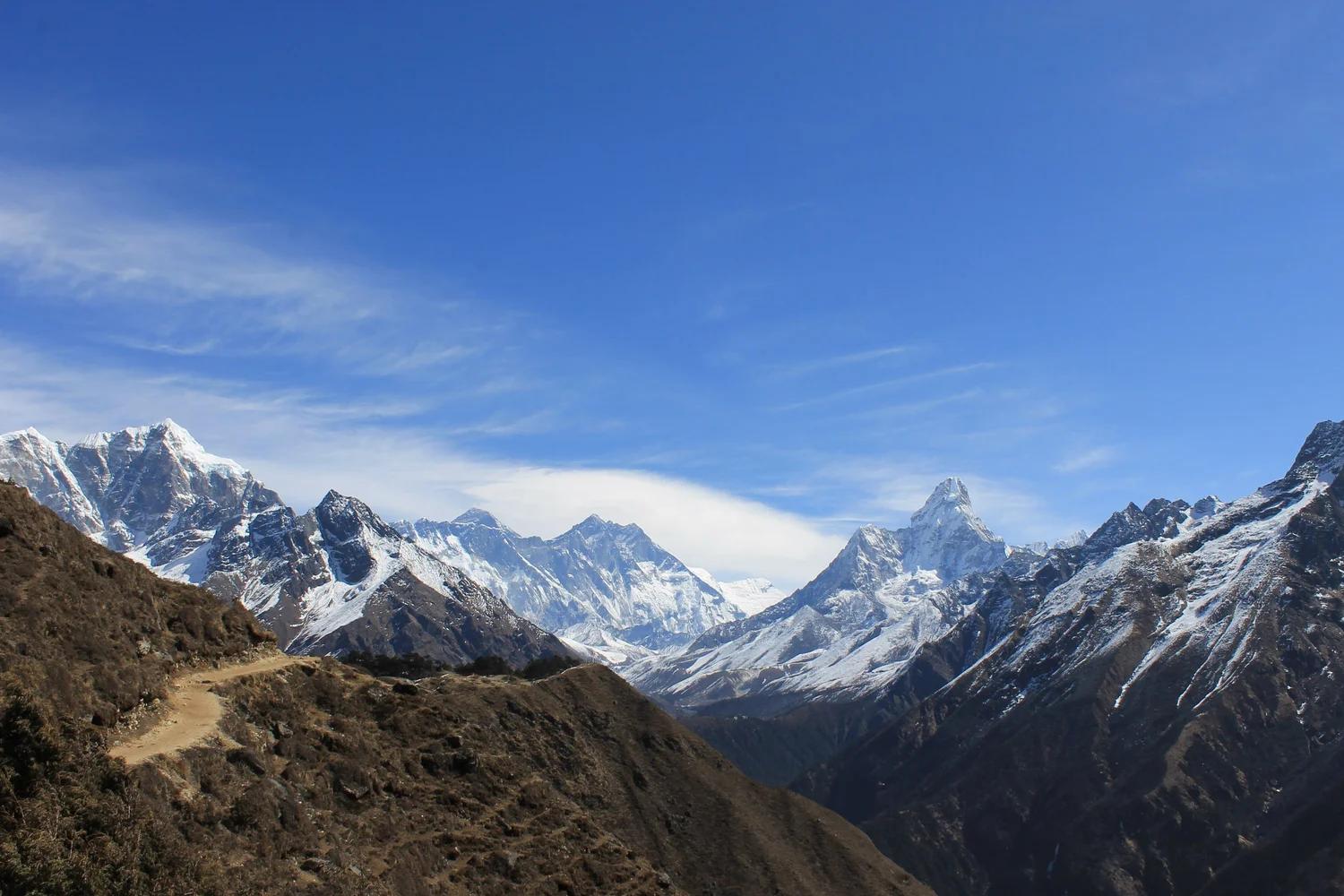 Snow-covered Himalayan peaks above a ridge trail under a clear blue sky