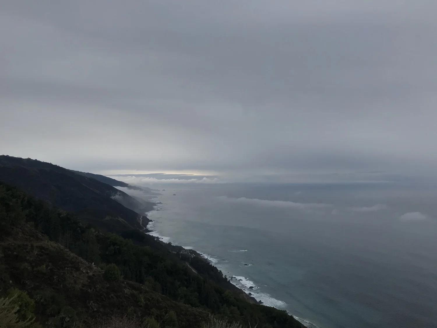 Fog settling over a rugged coastline and calm sea under a grey sky